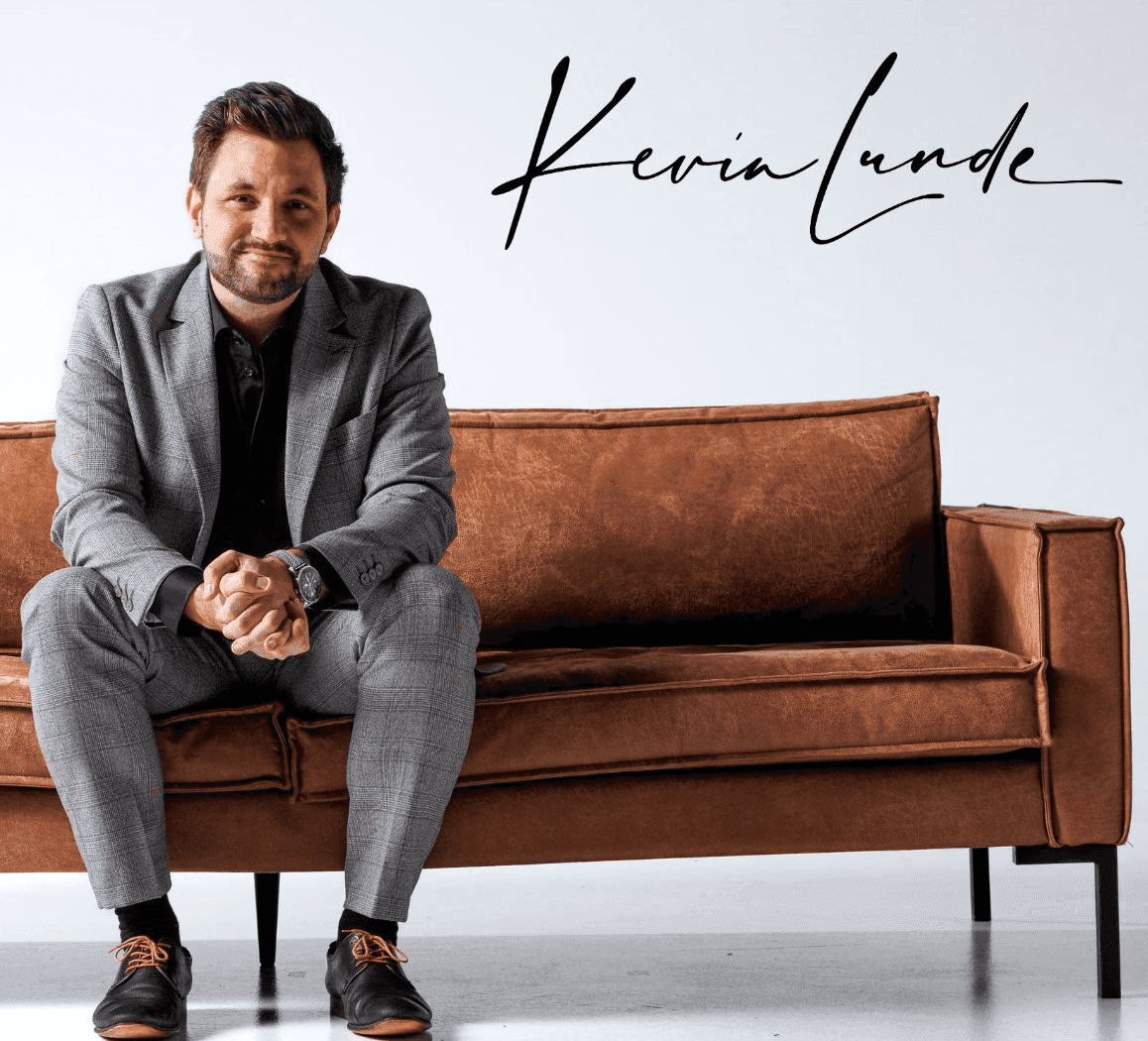 Kevin Lunde sittende i grå dress på en brun sofa, med signaturen sin over